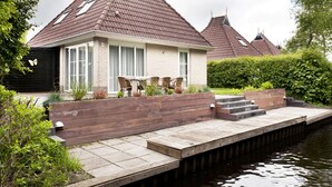 A house with a tiled roof, a wooden deck, and a water body in front. - Bungalowpark It Wiid by Interhome (Eernewoude)
