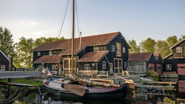 A traditional wooden house with a steep gabled roof, a dock with a rowboat, and a clear sky. - Bungalowpark It Wiid by Interhome (Eernewoude)