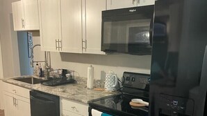 Una cocina moderna con armarios blancos, un refrigerador negro, un microondas y un lavavajillas.