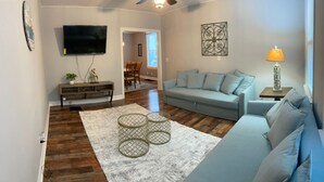 Una sala de estar con sofá, mesa de centro, televisión y lámpara.