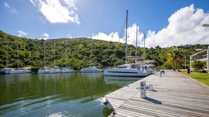A marina with boats docked along a wooden pier, surrounded by lush green hills. - Blue Sail Hotel SXM (Anse Marcel)
