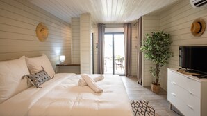 A bedroom with a bed, a TV, a plant, and a view to the outside. - Blue Sail Hotel SXM (Anse Marcel)