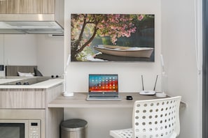 A modern kitchen with a laptop on a wooden countertop, a white chair, and a framed picture of a boat on water. - Coogee Studio Apartments (Coogee)