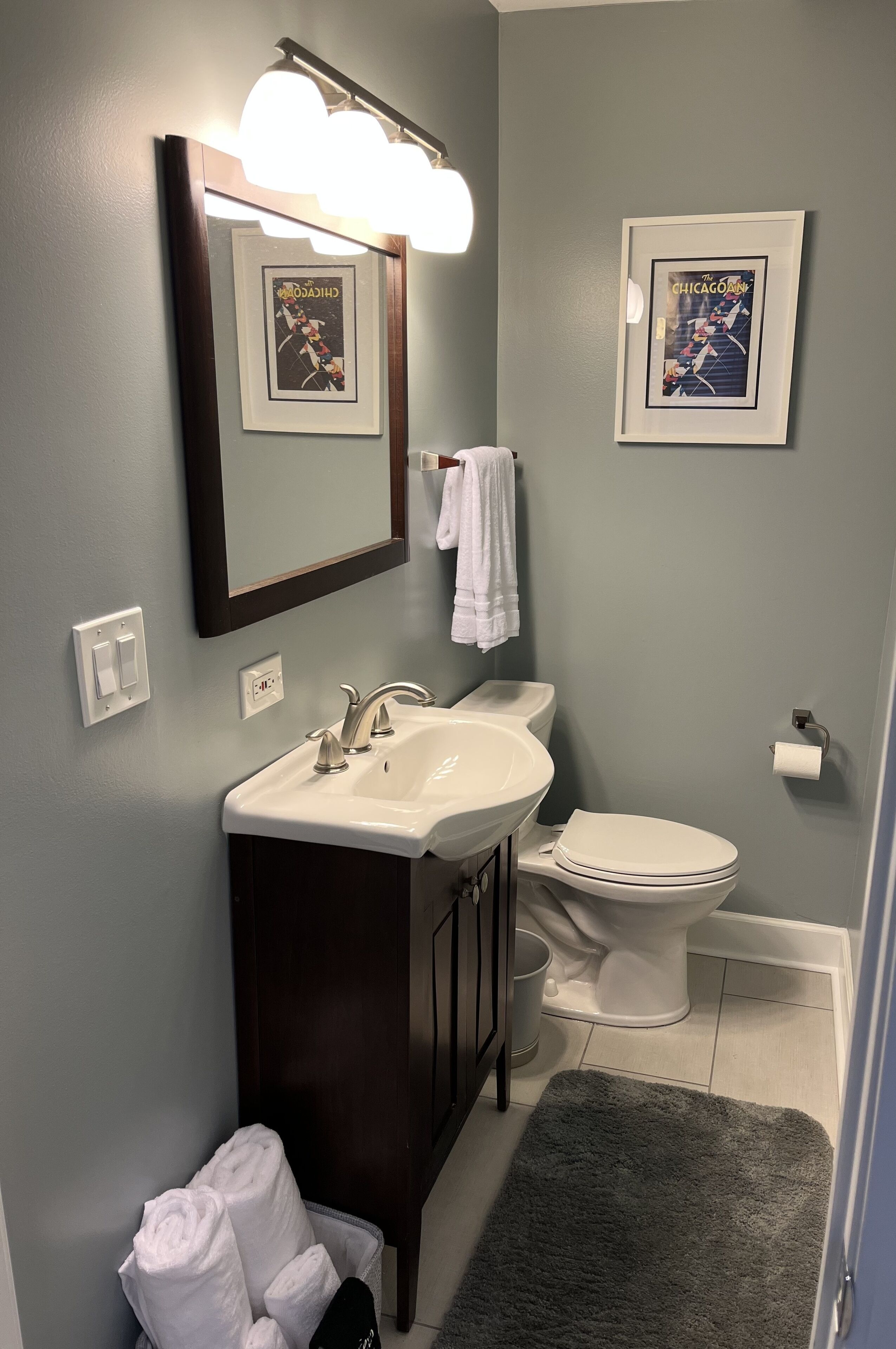 Une salle de bain avec un lavabo, un miroir et des toilettes. Des tableaux encadrés ornent le mur.