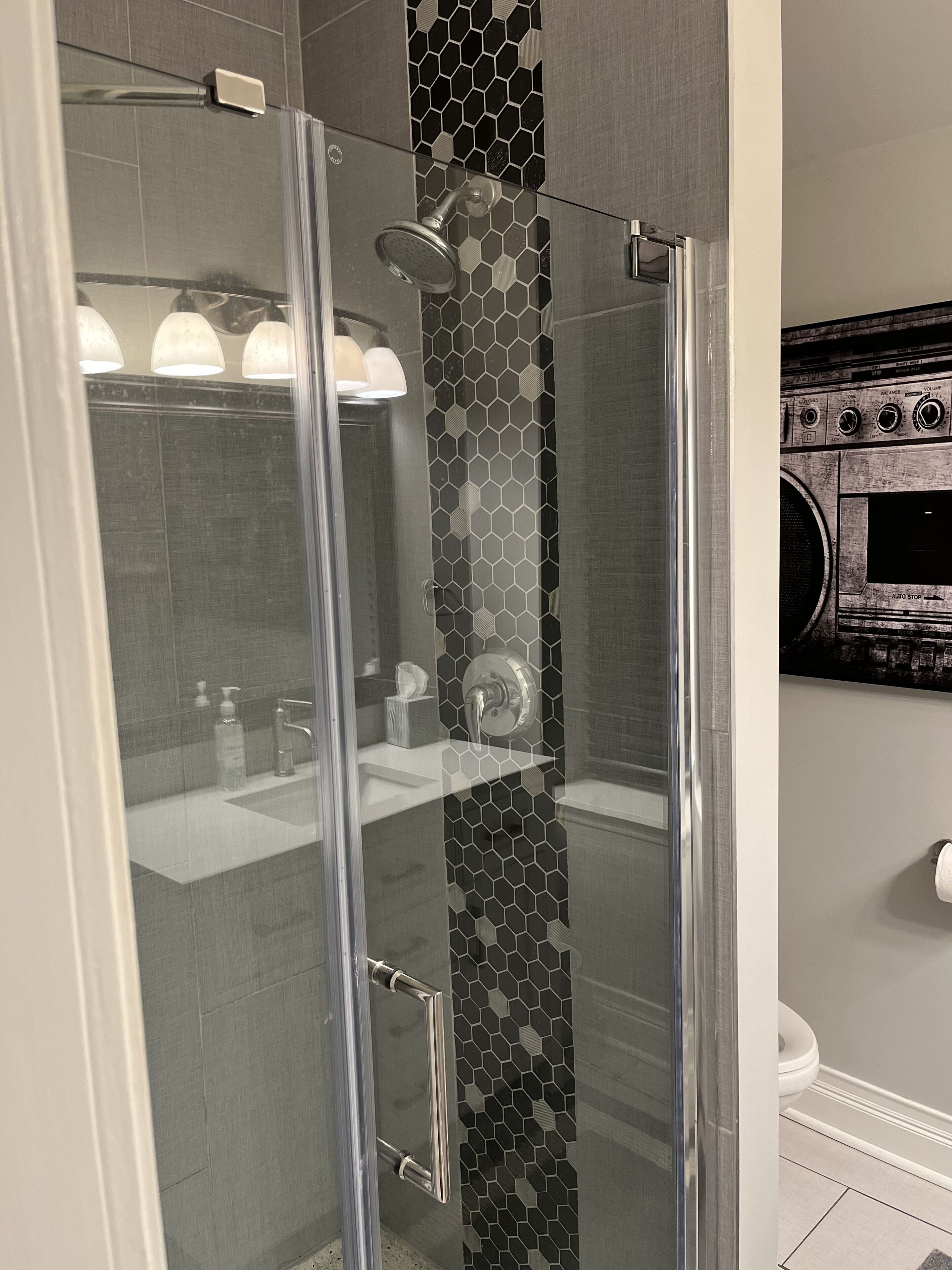 A modern bathroom with a glass shower enclosure, a white sink, and a black and white hexagonal tile backsplash.