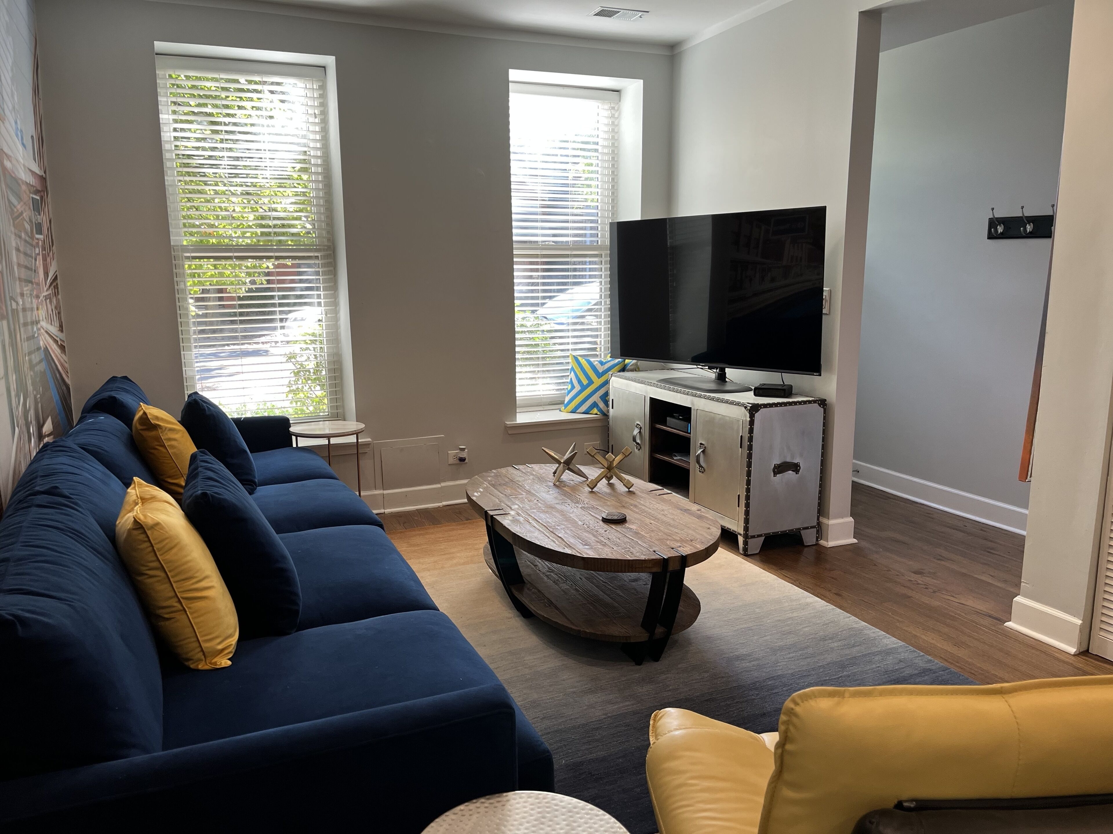 A living room with a blue sofa, a yellow armchair, a wooden coffee table, a flat-screen TV, and a cabinet with a TV on top.