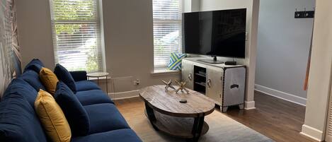 A living room with a blue sofa, a yellow armchair, a wooden coffee table, a flat-screen TV, and a cabinet with a TV on top.