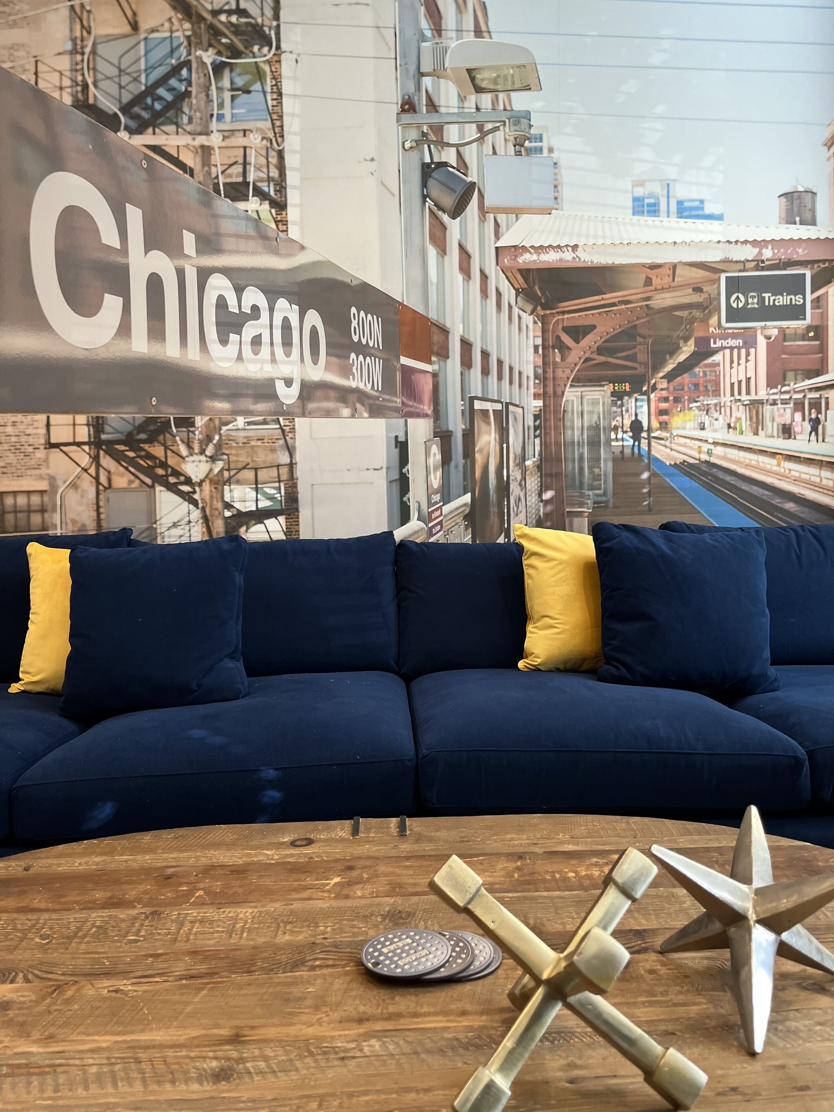 A blue sofa with yellow cushions in a room with a wooden table and a decorative metal sculpture.