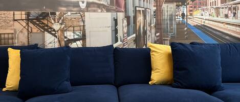 A blue sofa with yellow cushions in a room with a wooden table and a decorative metal sculpture.