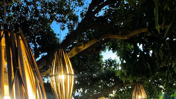 An outdoor seating area with wooden benches and tables, surrounded by trees and decorative hanging lights. - Hotel Pousada Villa Itália (Olímpia)
