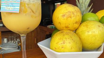 Een cocktailglas met een gele rietje en een briefje, een schaal met geel fruit, en een ananas op een houten tafel.