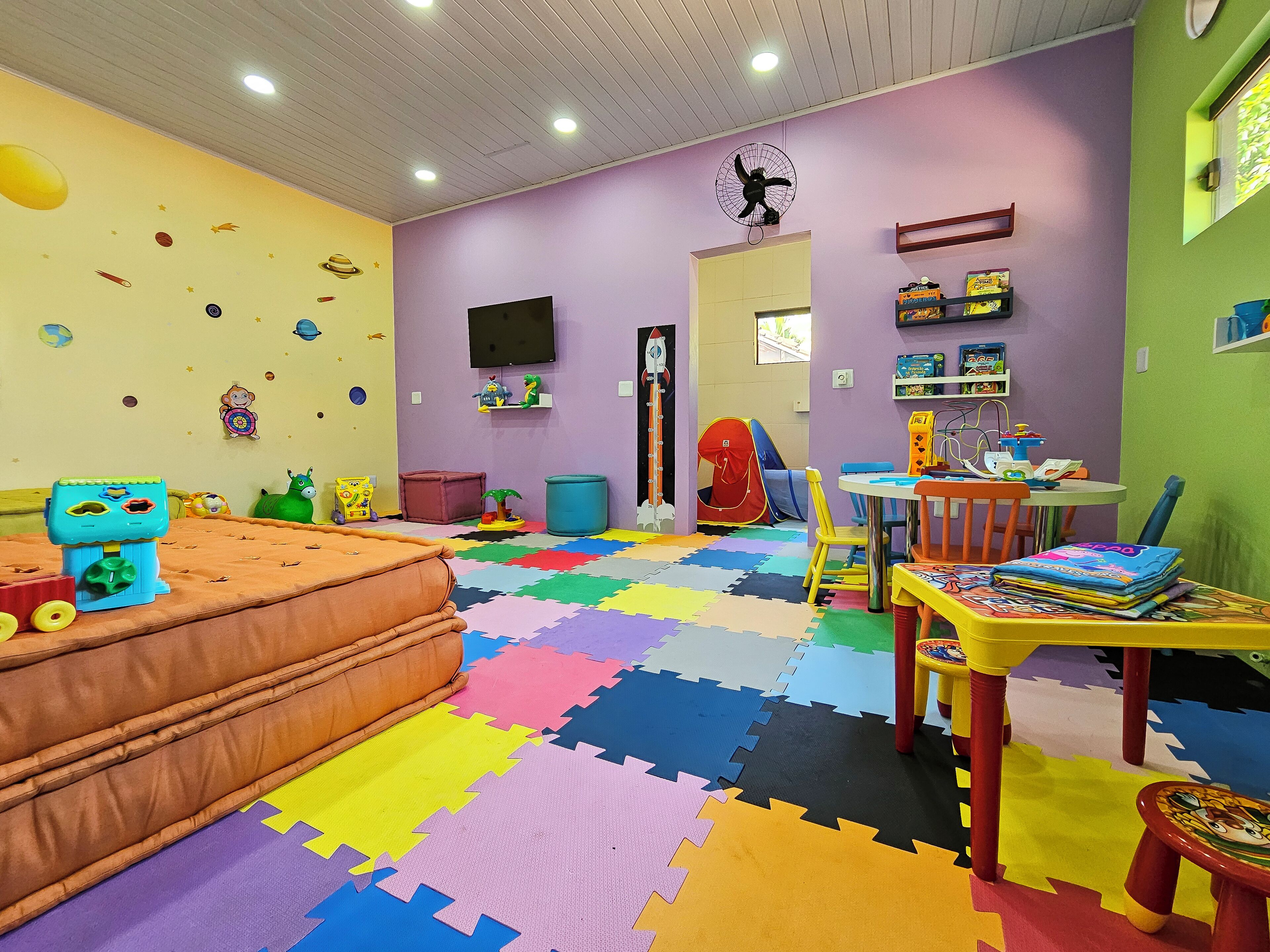 A children's playroom with colorful foam mats, a playhouse, and various toys.