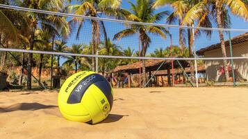 Un voleibol de playa sobre una cancha arenosa con una red, rodeado de palmeras y una estructura con techo de paja.