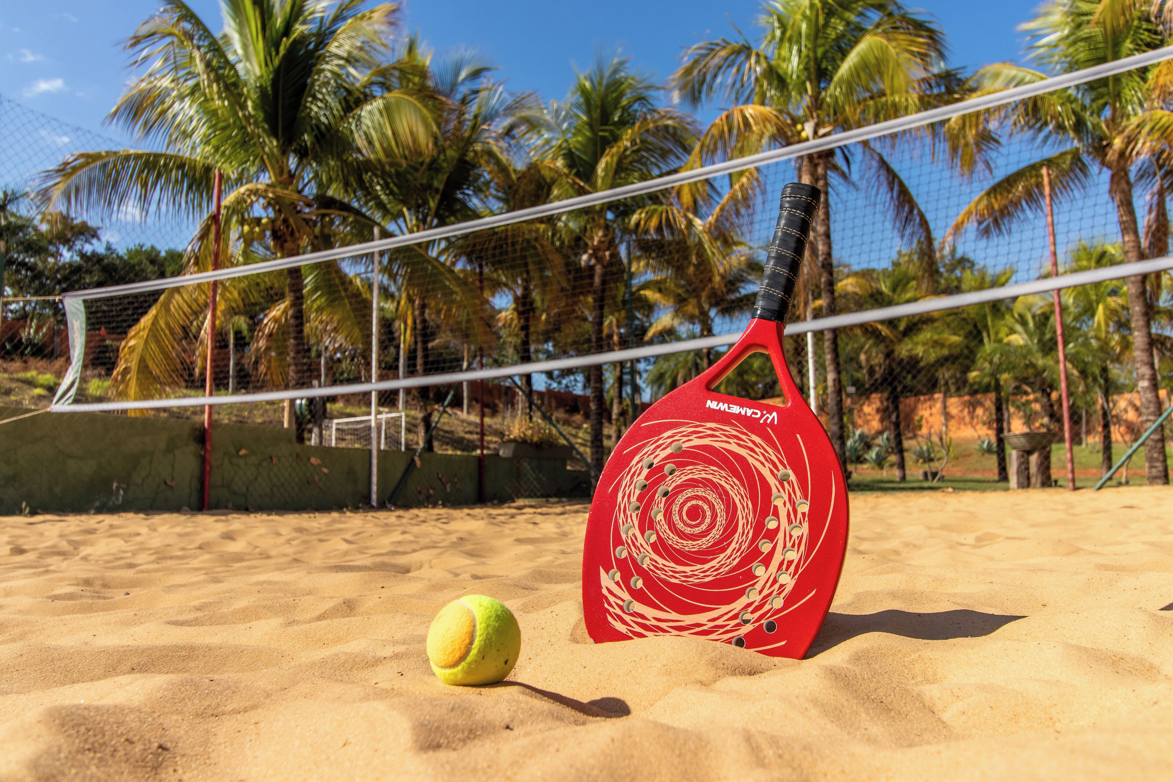 A beach volleyball court with a net, a red volleyball, and a red paddle.