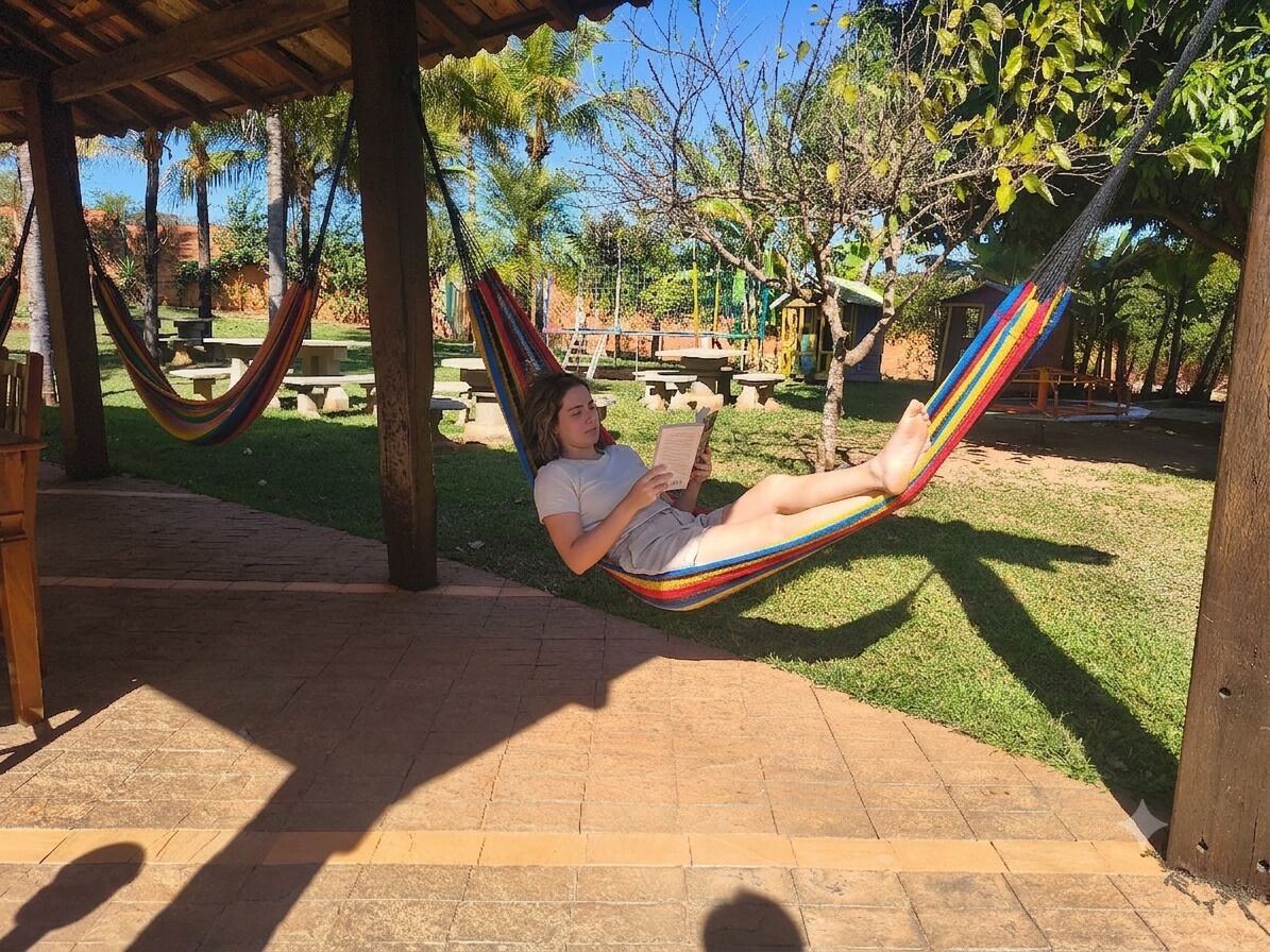 A hammock under a wooden structure with a grassy area and picnic tables in the background.