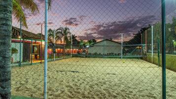 A fenced tennis court with a sandy surface, surrounded by a chain-link fence and palm trees.