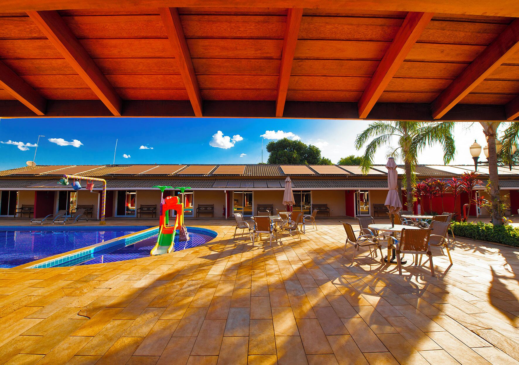 A covered pool area with a slide, outdoor seating, and a building with a tiled roof.