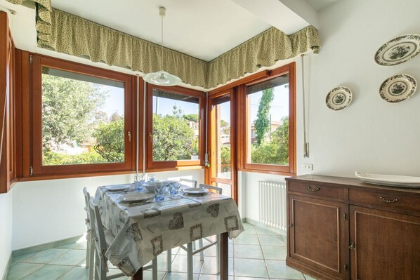 Uma sala de jantar com uma mesa posta para quatro pessoas, janelas amplas e um armário de madeira.