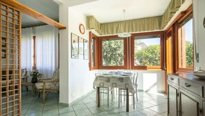 A dining area with a table set for four, a wooden chair, a window with curtains, and a clock on the wall. - Villa Luia by MMega Villas  (Marina di Pietrasanta)