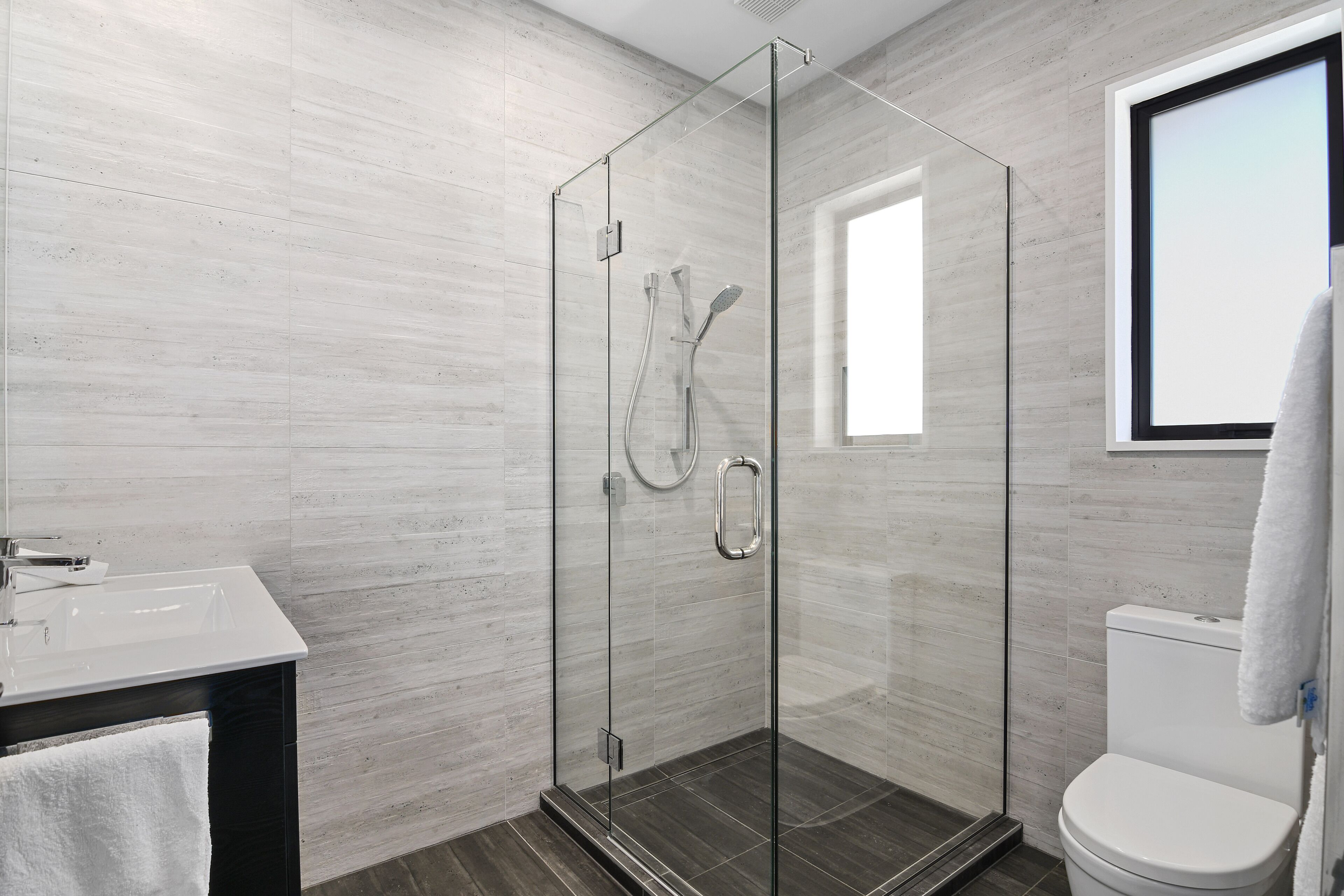 Een moderne badkamer met een glazen douchecabine, een witte wastafel en een toilet.