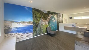 Zona de recepción con un gran mural de un paisaje costero, un mostrador de recepción y un área de estar.