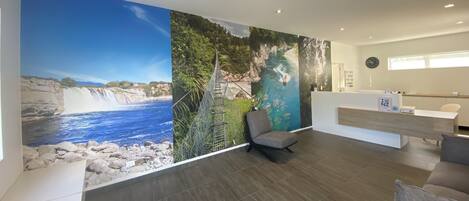 Zona de recepción con un gran mural de un paisaje costero, un mostrador de recepción y un área de estar.