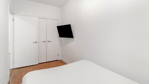 A bedroom with a bed, a white wardrobe, and a flat-screen TV mounted on the wall.