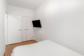 Une chambre à coucher avec un lit, une armoire blanche et un téléviseur à écran plat fixé au mur.