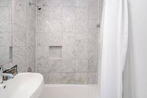 Uma casa de banho com uma pia branca, chuveiro e parede revestida a azulejos.