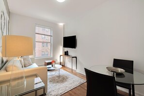 A modern living room with a sofa, coffee table, and a glass dining table. - Walk to Central Park | UES Retreat | Pet-Friendly (New York)