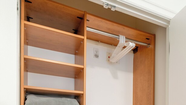 A wooden closet with multiple shelves and hanging space, a white laundry basket, and a white towel on the top shelf.