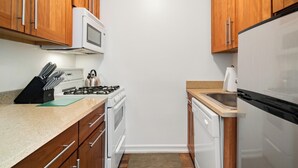 A compact kitchen with wooden cabinets, a gas stove, a microwave, and a dishwasher.