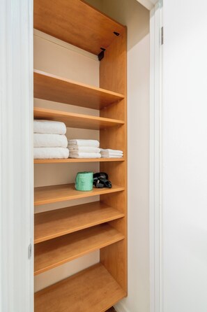 A wooden shelving unit with folded white towels and a green container. - Walk to Central Park | UES Retreat | Pet-Friendly (New York)