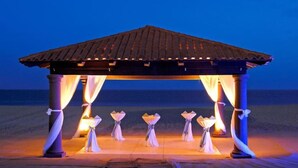 A beach gazebo with a tiled roof and draped curtains, illuminated by warm lighting.