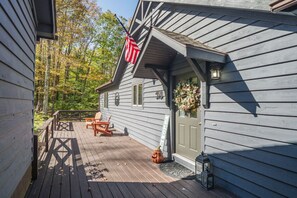 A wooden deck with Adirondack chairs, a door with a flower wreath, and an American flag.