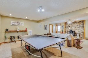 A room with a ping pong table, a fireplace, a ski patrol sign, and a Christmas tree.