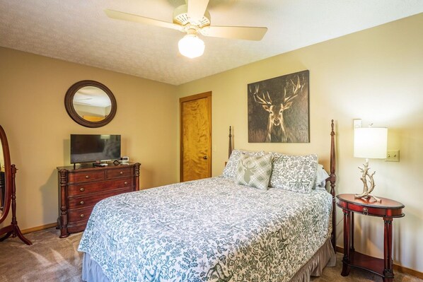 A bedroom with a bed, a dresser, a television, a mirror, a door, and a wall-mounted lamp.