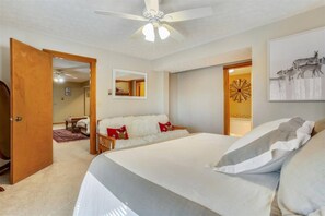 A bedroom with a large bed, a ceiling fan, a white fluffy sofa, and a door leading to another room. - Mtn Retreat w/ Fireplace & Game Room - Lazy Bear (Davis)