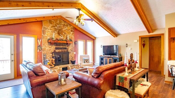 Ein gemütliches Wohnzimmer mit Kamin aus Stein, Ledersofas, einem Fernseher und einer Holzbalkendecke.