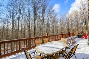 A snow-covered deck with a round table and chairs, surrounded by a wooden railing, overlooking a forest. - Mtn Retreat w/ Fireplace & Game Room - Lazy Bear (Davis)