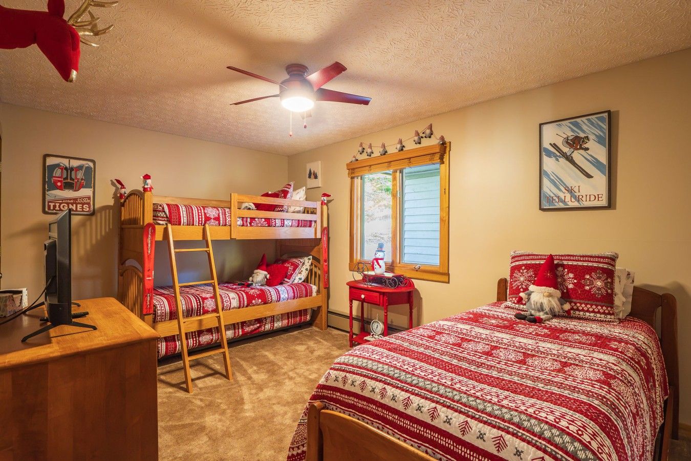 A room with bunk beds, a desk, a computer, a window with a view, and a ceiling fan.