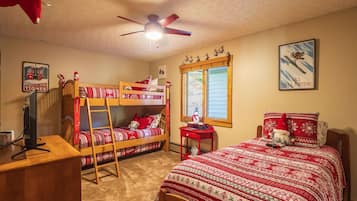 A room with bunk beds, a desk, a computer, a window with a view, and a ceiling fan.