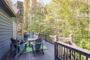 Una terraza de madera con mobiliario exterior, un muro de piedra y un fondo de bosque.