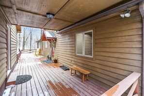 Una terraza de madera con un banco y un espacio de estar cubierto, una ventana con contraventanas y una puerta.