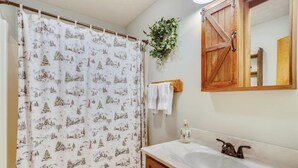 Ein Badezimmer mit Duschvorhang, der eine Winterlandschaft zeigt, einem Holzschrank, einem Spiegel und einer Pflanze an der Wand.