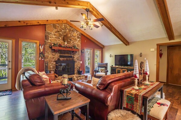 A cozy living room with a stone fireplace, leather sofas, a wooden coffee table, and a television.