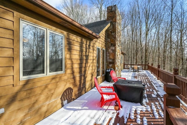 A wooden cabin with a deck, two windows, and a stone chimney.