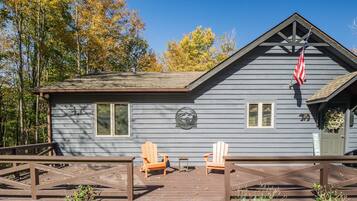 A cabin with a deck, two Adirondack chairs, and an American flag.