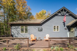 A cabin with a deck, two Adirondack chairs, and an American flag.