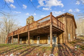 A wooden cabin with a stone chimney, a covered porch, and a view of a forested area. - Mtn Retreat w/ Fireplace & Game Room - Lazy Bear (Davis)